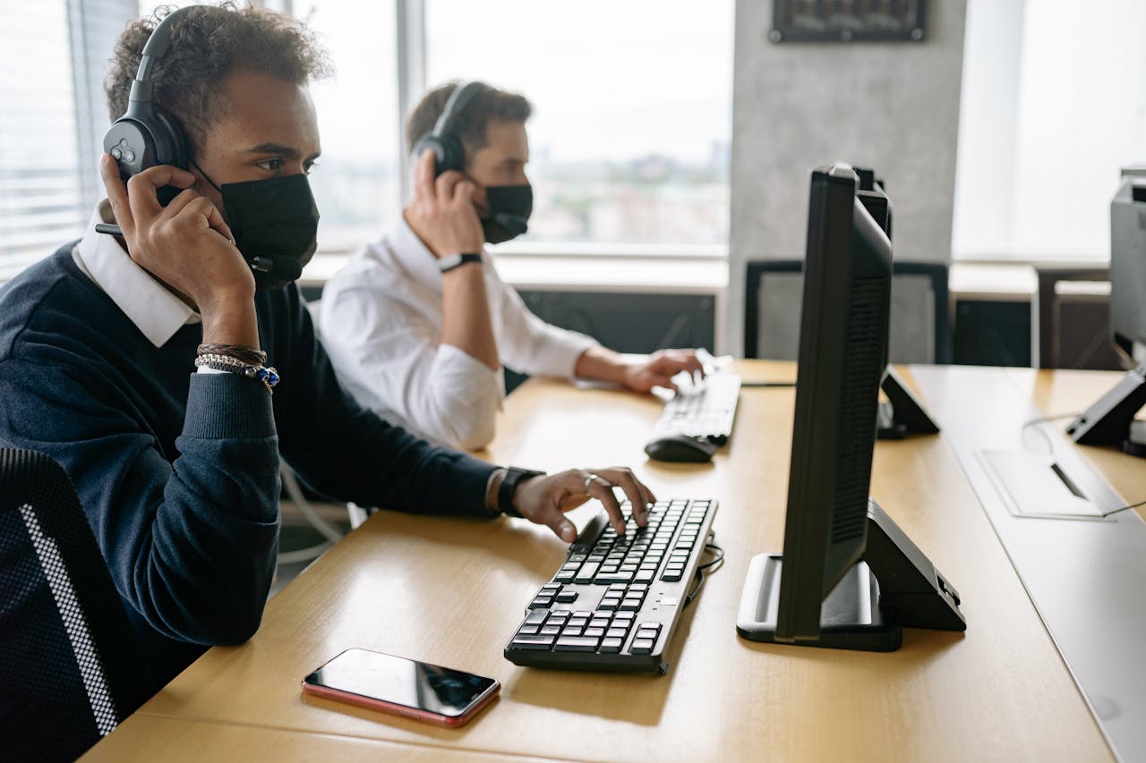 Two call center agents wearing face masks working on computers in a modern office.